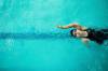 Rückenschwimmerin mit Schwimmbrille und schwarzem Badeanzug im Schwimmbecken, von oben betrachtet