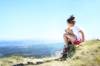 Mädchen sitzt auf einer Bergkuppe mit spektakulärem Ausblick und verarztet mit kleiner Reiseapotheke ihr Knie