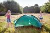 Zwei junge Frauen bauen auf einer Wiese ein grünes Zelt auf