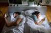 Paar mit T-Shirts bekleidet, liegt im Bett, sich gegenseitig abgewandt und schaut auf ihr Smartphone