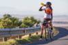 Rennradfahrerin hat an Leitplanke einer Strasse Halt gemacht und nimmt einen kräftigen Hieb aus ihrer Trinkflasche