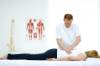 Chiropraktiker bearbeitet mit beiden Händen den Rücken einer auf dem Bauch liegenden Frau