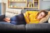 Frau liegt mit Bauchschmerzen auf Sofa