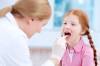Ärztin untersucht an rothaarig-gezopftem Mädchen Zunge und Rachen