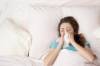 Frau liegt erkältet im Bett und schnäuzt sich die Nase