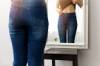 Frau in Jeans vor Spiegel fühlt ihren Bauch